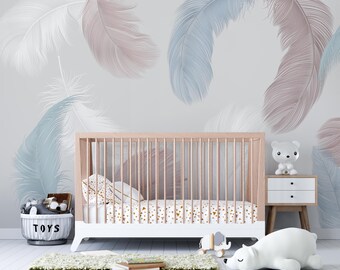 May include: A nursery scene featuring a white and natural wood crib with a patterned sheet and pillows. The room has a light gray wall with large feather designs in white, pink, and blue. A white side table, a toy basket, and a rug complete the decor.