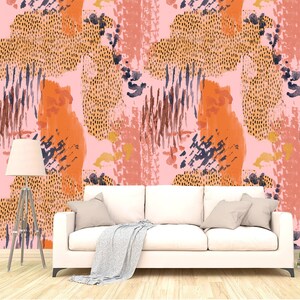 May include: A white sofa with a throw blanket sits in front of a pink wall with an abstract pattern of orange, brown, and black brushstrokes and dots.