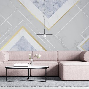 Peut inclure: Salon moderne avec un canapé sectionnel rose clair, un pouf assorti, une table basse ronde noire et une grande plante en pot. Le mur est orné d'un motif géométrique en marbre gris, blanc et or. Le canapé mesure environ 2,5 mètres.