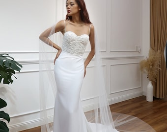 May include: A white wedding dress with a fitted bodice and a flowing skirt. The dress has a lace overlay on the bodice and a tulle train.