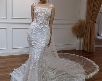 Può includere: Un abito da sposa bianco con un corpetto aderente e una gonna fluida. L'abito è ricoperto di delicati ricami floreali e paillettes.