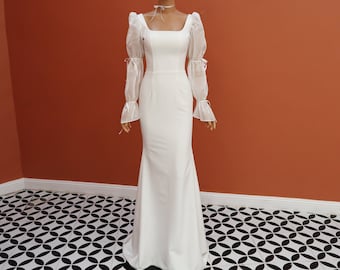 May include: A white wedding dress with a square neckline and long sleeves. The sleeves are made of a sheer fabric with a puff at the shoulder. The dress has a fitted bodice and a flowing skirt.