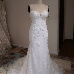 May include: A white strapless wedding dress with a fitted bodice and a flowing skirt. The dress is adorned with delicate floral appliques and sequins.