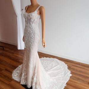 May include: A white wedding dress with a fitted bodice and a flowing skirt. The dress is covered in delicate floral lace and has a sweetheart neckline.