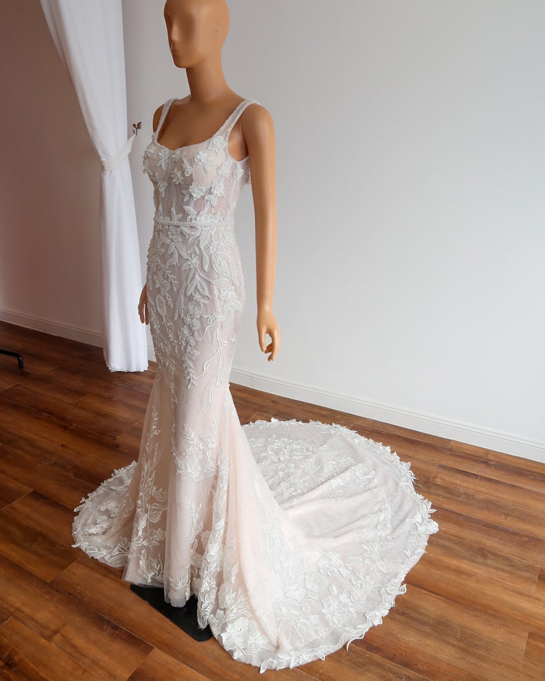 May include: A white wedding dress with a fitted bodice and a flowing skirt. The dress is covered in delicate floral lace and has a sweetheart neckline.