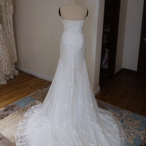 May include: A white strapless wedding dress with a fitted bodice and a flowing skirt. The dress is covered in delicate lace and sequins.