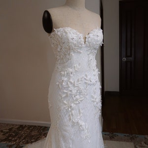 May include: A white strapless wedding dress with a fitted bodice and a flowing skirt. The bodice is adorned with intricate floral embroidery and sequins. The skirt is made of a soft, flowing fabric.