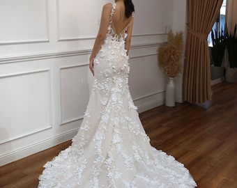 Può includere: Un abito da sposa bianco con un corpetto aderente e una gonna fluida. L'abito è ricoperto di delicati ricami floreali.