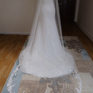 May include: A white bridal veil with a delicate floral lace trim. The veil is made of soft tulle and has a long, flowing design.