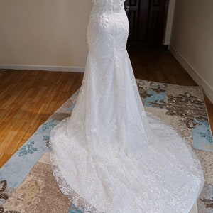 May include: A white strapless wedding dress with a fitted bodice and a flowing skirt. The dress is adorned with delicate lace and sequins.