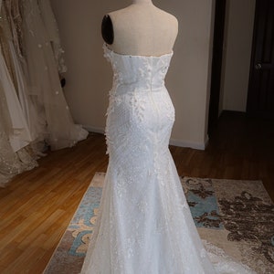 May include: A white strapless wedding dress with a fitted bodice and a flowing skirt. The dress is adorned with delicate lace and sequins.