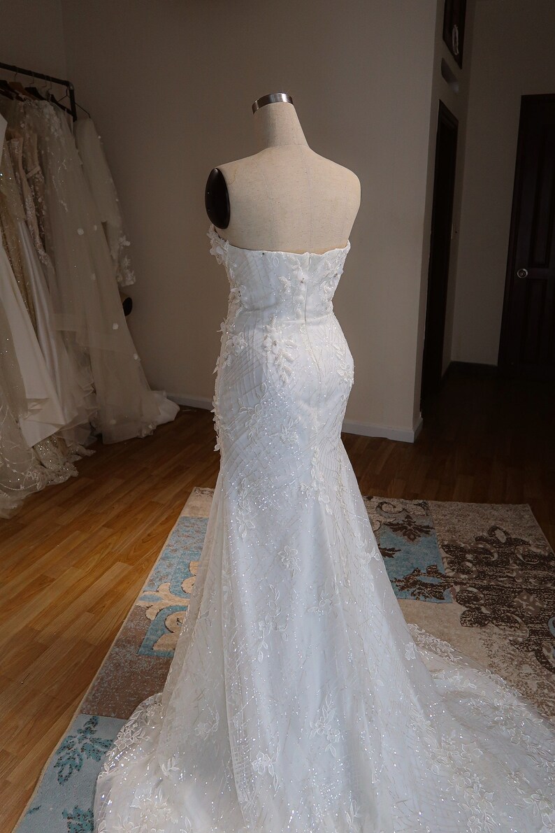 May include: A white strapless wedding dress with a fitted bodice and a flowing skirt. The dress is adorned with delicate lace and sequins.