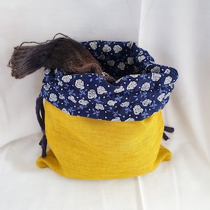 Könnte beinhalten: Eine gelbe Kordeltasche mit einem blauen und weißen Blumenmusterfutter. Die Tasche ist aus einem weichen, strukturierten Stoff gefertigt und hat einen Kordelverschluss.