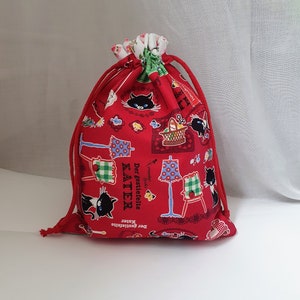 Könnte beinhalten: Rote Kordelzugtasche mit einer schwarzen Katze und einem Blumenmuster. Die Tasche trägt den Text "Der gestiefelte KATER".