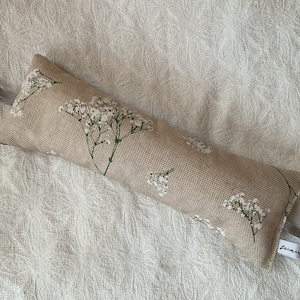 Peut inclure: Un cale-porte beige avec un motif floral blanc et une poignée en boucle grise. Le cale-porte a une petite étiquette avec le mot "Leinen" dessus.