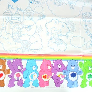 May include: A white tablecloth with a rainbow border and a scene of Care Bears in a cloud-filled sky. The Care Bears are lined up at the bottom of the tablecloth, each with their signature symbol and colors. The text "Care Bears" and "and related trademarks TM & &copy; 2004 Those Characters From Cleveland LLC. Licensed under license to Prima Party"