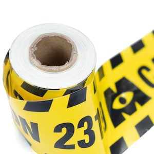 May include: A roll of yellow caution tape with black diagonal stripes and the number 23 printed in black. The tape is unrolled, revealing the text "CAUTION" and an eye symbol.