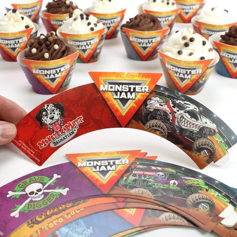 May include: A set of Monster Jam cupcake wrappers featuring different monster trucks, including Grave Digger, Monster Mutt Dalmatian, and El Toro Loco. The wrappers are red, orange, purple, and green with black and white details.
