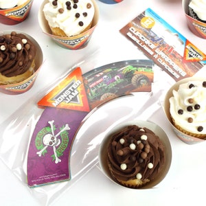 May include: Monster Jam themed cupcake wrappers and cupcakes. The wrappers feature a monster truck design with the words "Grave Digger" and "Monster Jam". The cupcakes are decorated with chocolate and white frosting and chocolate sprinkles.