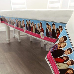 May include: A white plastic tablecloth with a blue and pink border featuring a Friends TV show theme. The border has a repeating pattern of pink zigzags and a blue background with images of the Friends cast members. The border also includes the text "Friends 2010".