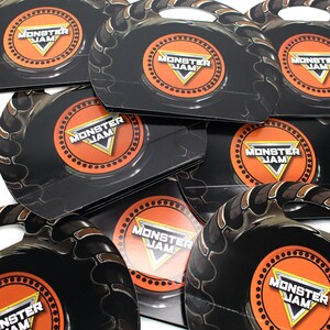 May include: A stack of black and orange Monster Jam party favor boxes with a tire tread design. Each box features a Monster Jam logo with the text "Monster Jam".