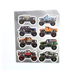 May include: A sheet of stickers featuring various monster truck designs. The trucks are in vibrant colors, including orange, green, blue, and red, with detailed graphics. Each truck has large tires and unique themes, such as a shark, skull, and zombie.