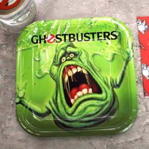 May include: Green paper party plate with a green ghost with a big mouth and red teeth. The ghost is surrounded by green slime. The text "Ghostbusters" is printed in black at the top of the plate.
