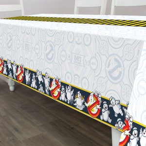 May include: White plastic tablecloth with a black and yellow striped border. The tablecloth features a repeating pattern of a ghostbuster logo and the words "Ray's Ghostbusters" in a circle. The border features a repeating pattern of ghosts and a "no ghosts" sign.