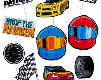 May include: A collection of racing-themed cutouts, including two race cars, two helmets, a tire, a speedometer, a checkered flag, and signs that read "DAYTONA INTERNATIONAL SPEEDWAY", "NASCAR", and "DROP THE HAMMER!".