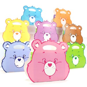 May include: A set of nine colorful paper gift bags featuring Care Bear characters. Each bag has a different color and a different Care Bear face with a heart on its chest. The bags have handles and are perfect for holding small gifts.