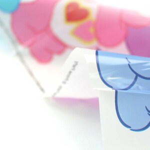 May include: Close-up of a clear plastic sheet with a pink and blue cartoon character design. The sheet is folded in half, revealing the design on both sides.