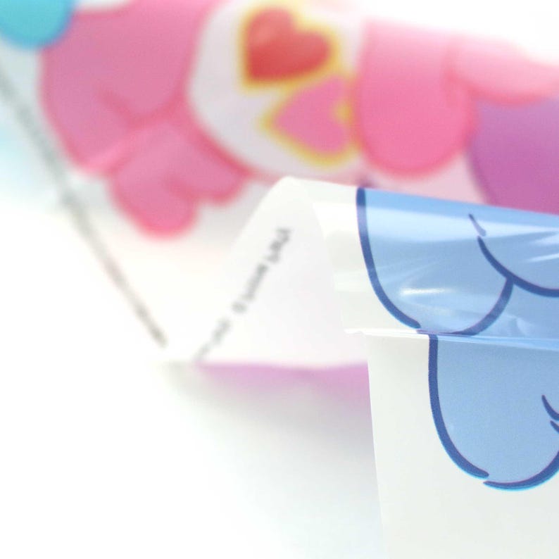 May include: Close-up of a clear plastic sheet with a pink and blue cartoon character design. The sheet is folded in half, revealing the design on both sides.