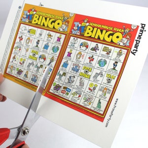 Puede incluir: Dos tarjetas de bingo rojas y amarillas con el t&iacute;tulo "Schoolhouse Rock Bingo". Las tarjetas est&aacute;n llenas de frases de la popular serie de televisi&oacute;n educativa. Las tarjetas se est&aacute;n cortando con unas tijeras.