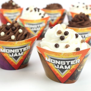 May include: Monster Jam themed cupcake wrappers with orange, purple, and brown designs. The wrappers feature a silver triangle with the words "Monster Jam" in black text. The cupcakes are topped with chocolate and white frosting and chocolate sprinkles.