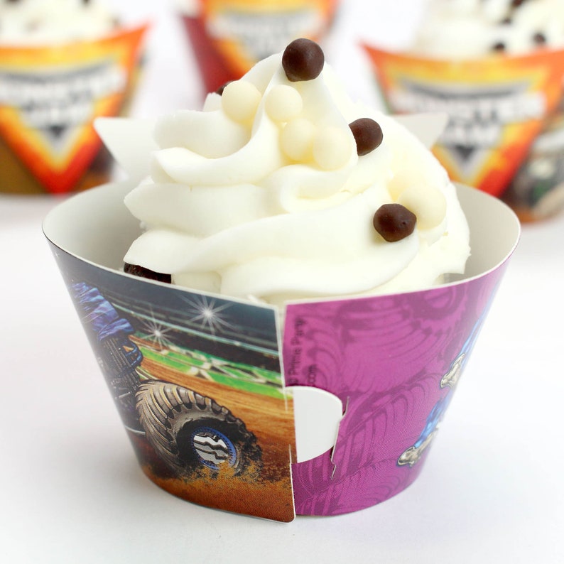 May include: A white cupcake with chocolate and white sprinkles in a purple and blue monster truck themed cupcake wrapper.