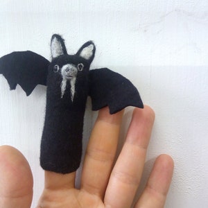Può includere: Un burattino a forma di pipistrello nero in feltro, con dettagli bianchi sulle orecchie e sul viso. Il pipistrello ha le ali spiegate ed è progettato per essere infilato su un dito. L'oggetto è fatto a mano.