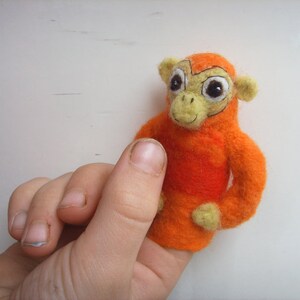 Könnte beinhalten: Orangefarbener Fingerpuppe aus Filz, die einen Affen mit schwarzen Augen und einer gelben Nase darstellt.
