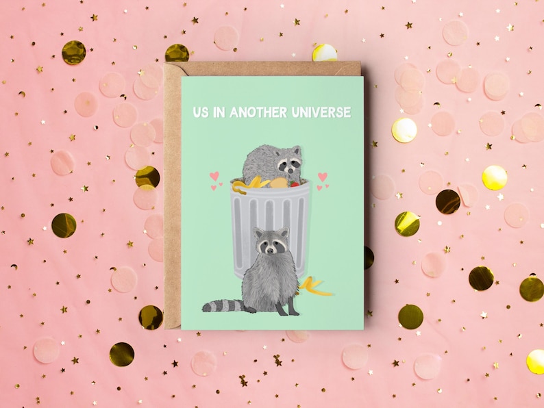 A green greeting card with an illustration of two raccoons and the text ''Us In Another Universe"