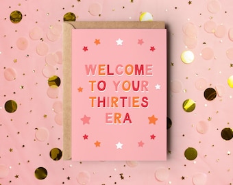 May include: A pink greeting card with the text "WELCOME TO YOUR THIRTIES ERA" in a colorful font, surrounded by star illustrations. The card is inside a brown envelope, set against a pink background with confetti.
