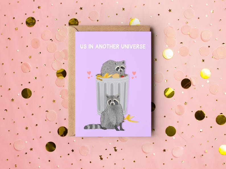 A purple greeting card with an illustration of two raccoons and the text ''Us In Another Universe"