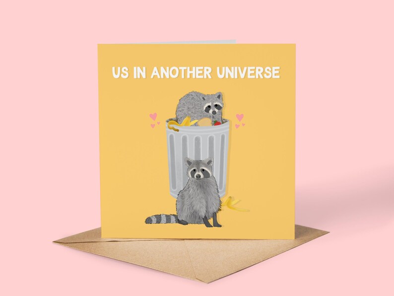 A yellow greeting card with an illustration of two raccoons and the text ''Us In Another Universe"