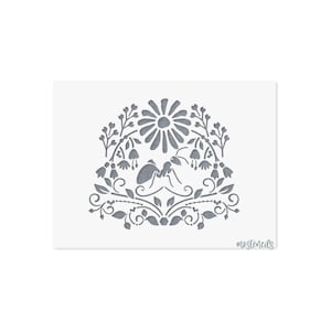 May include: A rectangular stencil featuring a gray cutout design of an ant centered beneath a large daisy flower, surrounded by symmetrical floral sprigs, leaves, and vines. The text "mostencils" is printed in the bottom right corner.