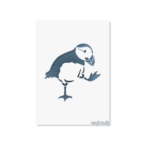 Könnte beinhalten: Eine Schablone mit der blauen Silhouette eines Papageientauchers, der auf einem Bein steht und einen Flügel hebt. Das Design hat ein dezentes Gittermuster in den blauen Bereichen und der Text "mostencils" steht in kleiner Schreibschrift unten rechts.