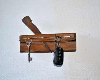 Può includere: Un pialla a mano in legno con una lama in metallo, utilizzata come portachiavi. Due chiavi e un portachiavi per auto sono appesi alla pialla.