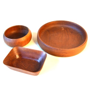 Puede incluir: Tres cuencos de madera, uno redondo y dos ovalados, hechos de madera oscura con un patrón de veta natural.