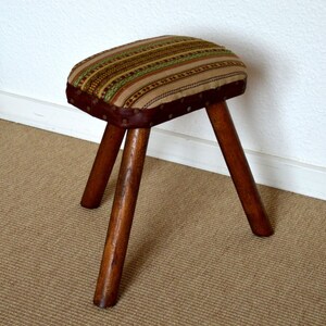 Vintage stool with 3 legs and woven fabric covering.