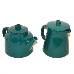 Pu&ograve; includere: Un set da t&egrave; in ceramica color verde acqua composto da una teiera e un lattiera. La teiera ha un corpo rotondo e un beccuccio. La lattiera ha un corpo alto e cilindrico.