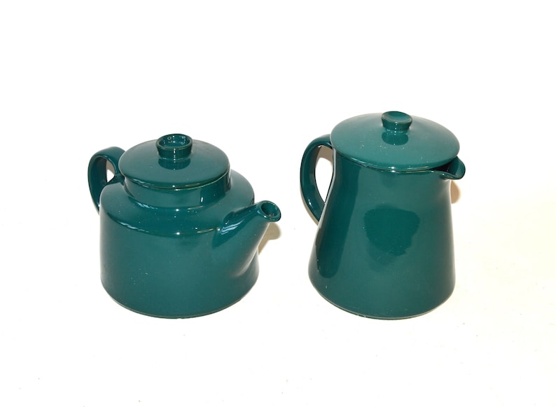 Pu&ograve; includere: Un set da t&egrave; in ceramica color verde acqua composto da una teiera e un lattiera. La teiera ha un corpo rotondo e un beccuccio. La lattiera ha un corpo alto e cilindrico.