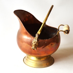 Può includere: Un secchio per carbone in rame e ottone con un manico in legno. Il secchio ha un corpo arrotondato e una base in ottone decorativa.