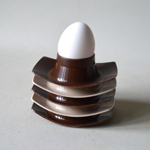 Peut inclure: Un ensemble de quatre supports à œufs en brun et beige empilés les uns sur les autres. Le support du haut contient un œuf blanc.